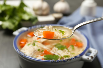 Spoon with fresh homemade chicken soup on blurred background, closeup