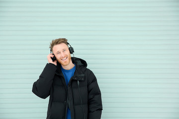 Young man listening to music with headphones against light wall. Space for text
