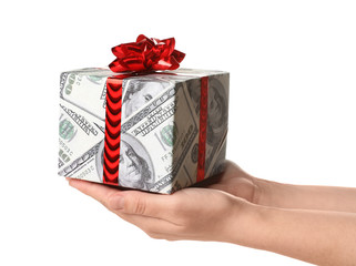 Woman holding gift box wrapped in decorative paper with dollar pattern on white background, closeup