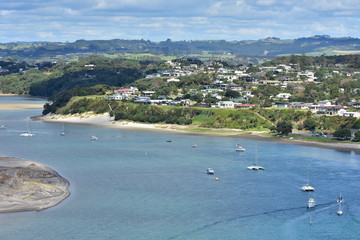 View of Mangawhai Harbour with moorings and sand dunes and dense housing of popular holiday destination of Mangawhai Heads.
