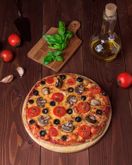 Traditional Italian vegetarian pizza with mushrooms, cherry tomatoes, black olives and basil on brown wooden table