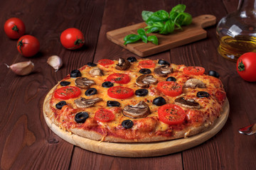 Traditional Italian vegetarian pizza with mushrooms, cherry tomatoes, black olives and basil on brown wooden table