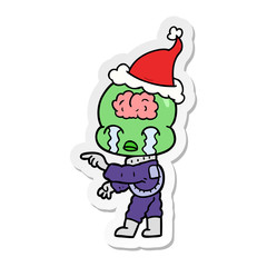 sticker cartoon of a big brain alien crying and pointing wearing santa hat