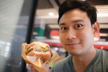 Funny face expression of Asian man eat a hamburger.