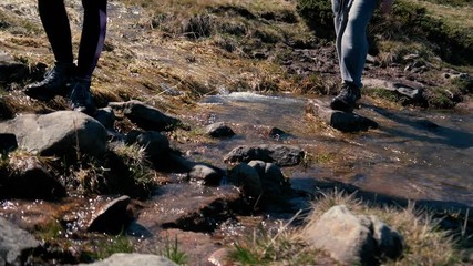 Slim female legs in boots crossing a mountain rill in the Carpathians in slo-mo