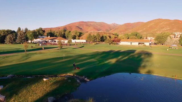 Drone Mid Height Zoom From Pond Past Crater To Mountains. Aerial shot as drone hovers toward the Homestead ponds with fountains, trees, golf course with players, carts, buildings and mountains.