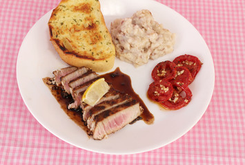 Overhead View of Tuna Steak in balzamic vinegar sauce and served with tomatoes and Potatoes.