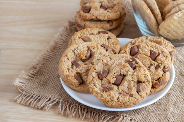 Chocolate chip cookies on white plate on brown sackcloth.