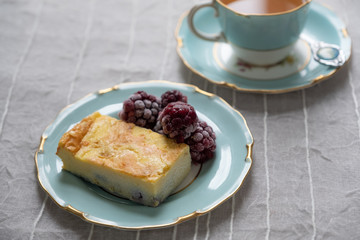 horizontal shot of baked cheesecake slice with berries and tea on decorative plate
