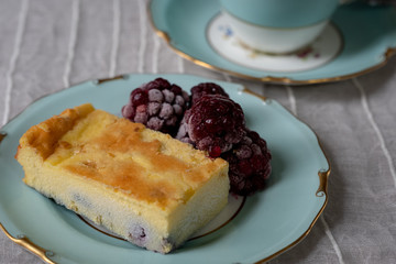 close up of baked cheesecake slice with berries and tea on decorative plate