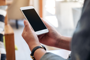 Mockup image of a hand holding white mobile phone with blank screen with coffee cup on wooden table in cafe