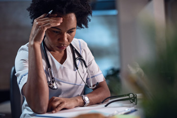 Worried black female doctor reading medical documents at the office.