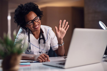 Happy African American doctor waving while making a video call over laptop.