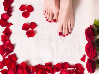 beautiful female feet with a red pedicure in a bath with salt and rose petals. Spa and skin care concept.