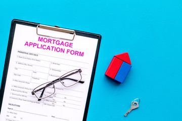 Mortgage concept. Mortgage application form near key and house made of constructor on blue...
