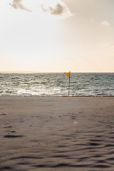 A yellow warning flag indicating adverse conditions on a tropical white sand beach.