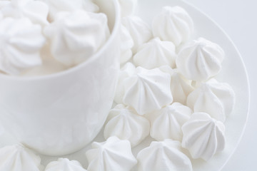 The side close up view of the white little meringue in the white tea cup on the white plate on white next to the white tea cup table and white background