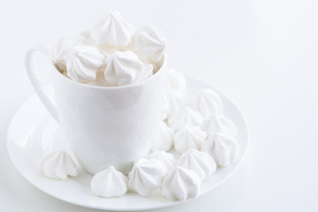 The side view of the white meringue in the white tea cup on the white plate on white table and white background