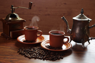 Two cups of hot coffee with steam, coffee grinder, coffee beans on the table