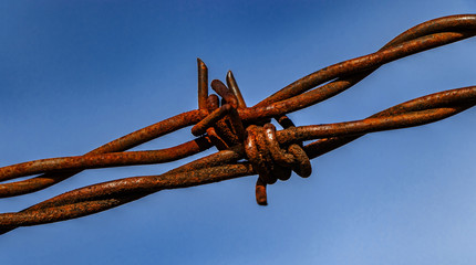 Rostiger Stacheldraht vor blauem Himmel