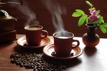 Two cups of hot coffee with steam, coffee grinder, coffee beans on the table
