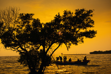 Silhouette of Fishermen on a Boat at Sunset Scene With Beautiful Tree Foreground. Fishery Lifestyle in Golden Hour at Gulf of Thailand.