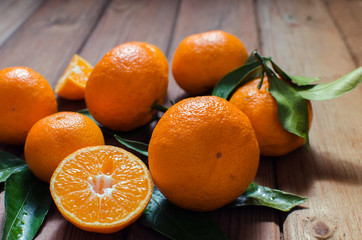 Fresh mandarin oranges fruit or tangerines with leaves in a plate on dark wooden table.