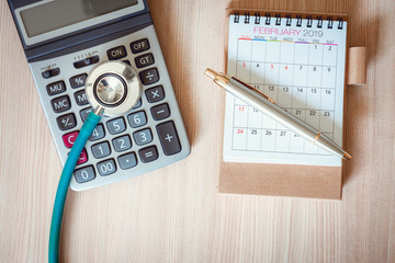 Business Healthcare Medicine and Insurance concept.Top view of stethoscope on calculator with calendar checkup concept., Annual doctor appointment for physical check-up against wooden background.