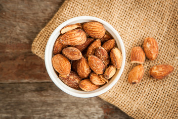 Close up Almonds with salted and Roasted in the white cup put on the sackcloth and wood floor, the great snack 