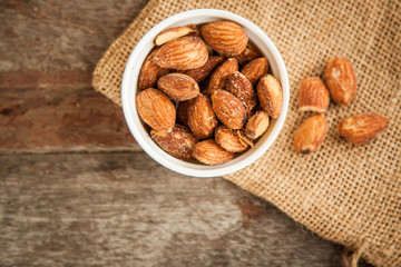Close up Almonds with salted and Roasted in the white cup put on the sackcloth and wood floor, the great snack 