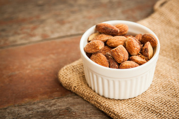 White cup of almonds on the sackcloth and old wood background 