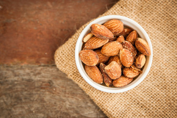 White cup of almonds on the sackcloth and old wood background 