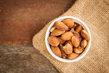 Close up Almonds with salted and Roasted in the white cup put on the sackcloth and wood floor, the great snack 