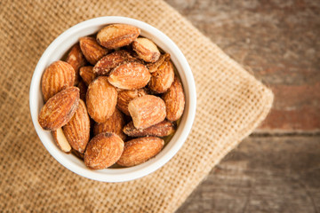Close up Almonds with salted and Roasted in the white cup put on the sackcloth and wood floor, the great snack 