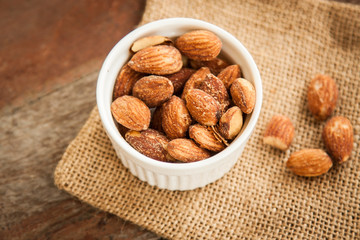 Close up Almonds with salted and Roasted in the white cup put on the sackcloth and wood floor, the great snack 