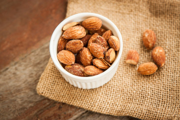 Close up Almonds with salted and Roasted in the white cup put on the sackcloth and wood floor, the great snack 