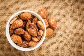 Close up Almonds with salted and Roasted in the white cup put on the sackcloth and wood floor, the great snack 