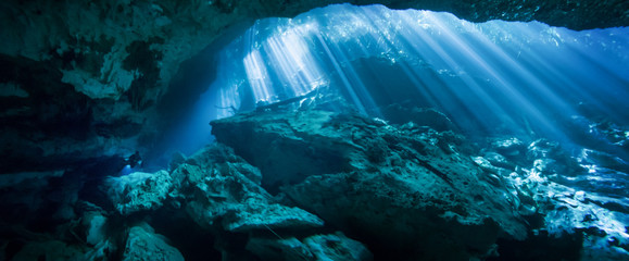 Sunlight shining through an opening in the El Jardin del Eden cenote with a scuba diver in the...