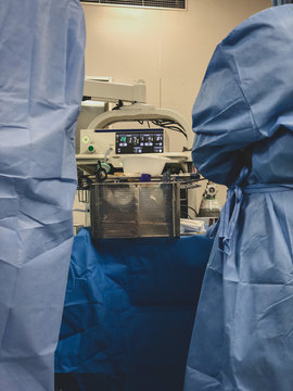 Surgeons using surgical instruments for keyhole surgery, watching the monitor which displays images from inside the patient's abdomen - operating theatre with lights in the background. 