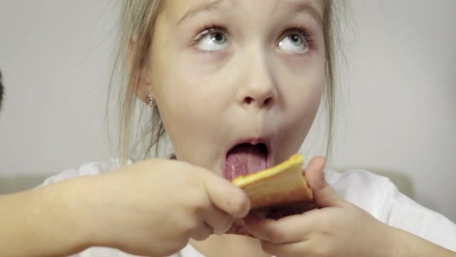 Close-up of baby's hand taking a piece of juicy, greasy pizza and bringing it to her mouth, funny girl in white t-shirt licks the treat, food and smiles. Unhealthy food concept. 4K resolution
