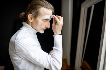 Actor putting mime makeup on his face preparing for perfomence indoors