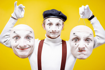 Portrait of a pantoomime holding two facial masks with different emotions on the yellow background....