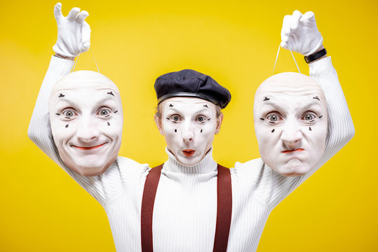 Portrait of a pantoomime holding two facial masks with different emotions on the yellow background. Concept of personality split
