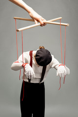Actor as a marionette controlled with ropes by a huge hand on the grey background. Concept of a...