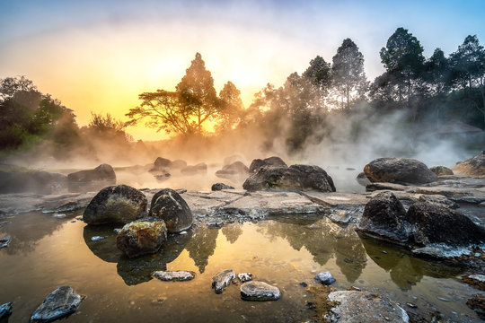 Chae Son National Park, Hot springs over rocky terrain with misty and morning sunrise rays of sun through branches of tree, Lampang Province, Thailand.