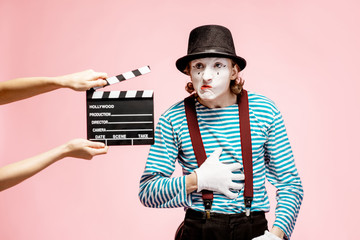 Portrait of an actor as a pantomime with cinematography clapperboard on the pink background