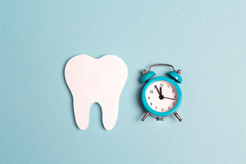 White paper tooth with alarm clock on blue background. Time to dental health. Flat lay, top view,...