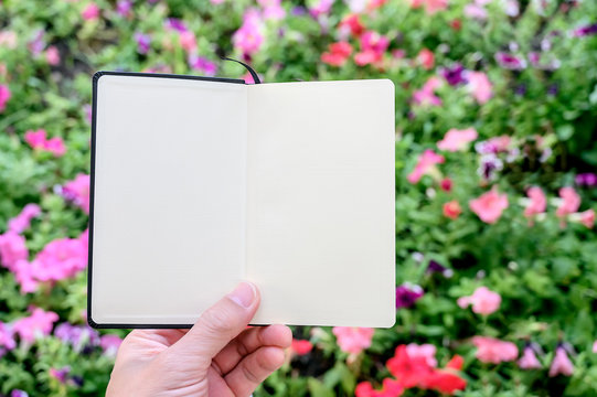 Shot photo of man hand holding blank page notebook with flower garden background.