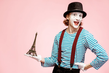 Pantomime with white facial makeup posing with Eiffel tower on the pink background. French mime...
