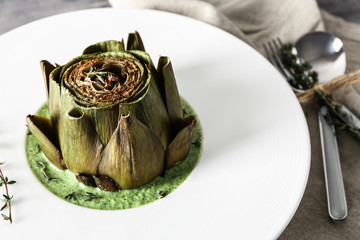 Plate with tasty cream soup and artichoke on table